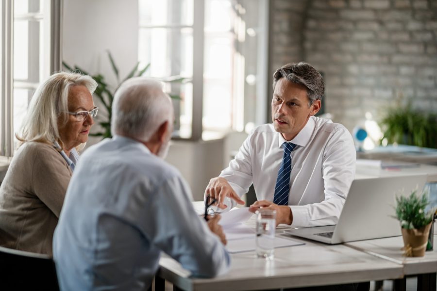 Mid adult insurance agent with mature couple analyzing financial reports and communicating during the meeting in the office.